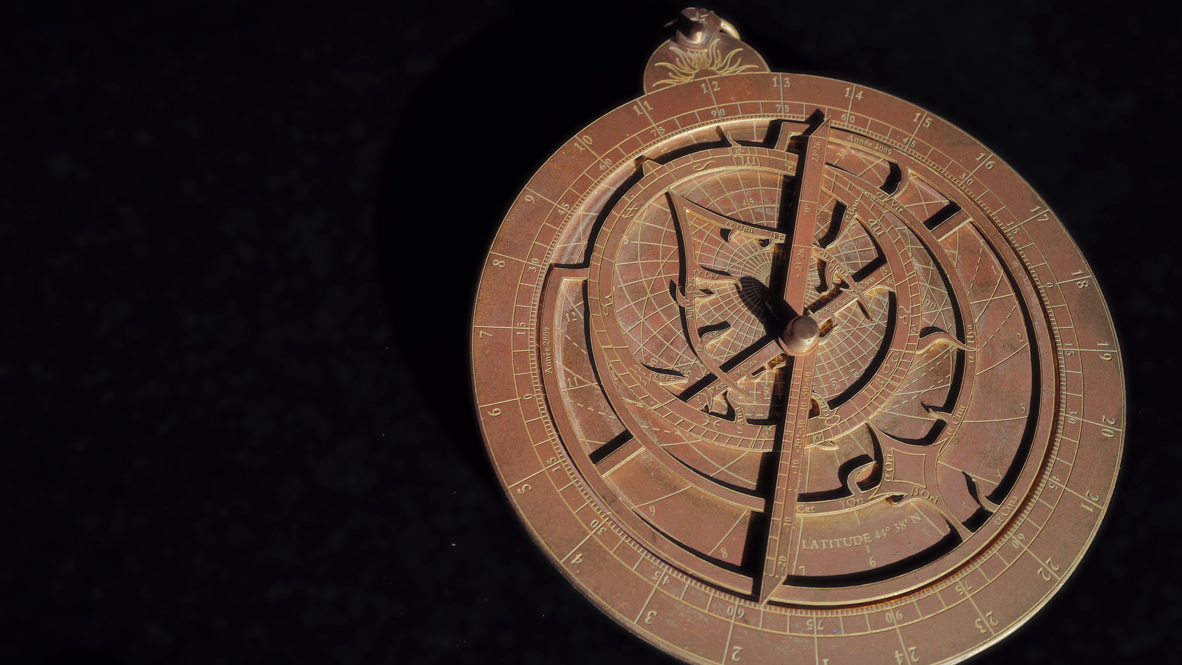 Brass astrolabe lit by sunlight on dark Zimbabwean granite — photograph by Philippe Robert.